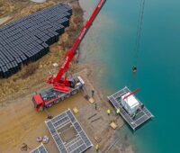 Ein Kran hievt einen Container auf eine künstliche Insel, Bauarbeiten für die schwimmende Solaranlage (Floating-PV) auf dem Kühlsee in Iffezheim.