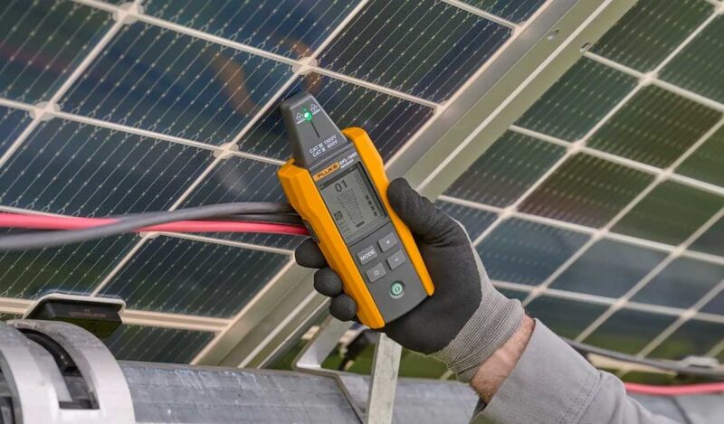 Ein Solartechniker hält das Erdschlussortungsgerät für Photovoltaik-Anlagen GFL-1500 von Fluke in einem Solarpark an ein PV-Modul.