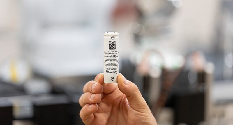 Eine Hand hält eine Rundzelle, das Fraunhofer IPA will umweltfreundliche Batteriespeicher auf LMFP-Basis entwickeln.