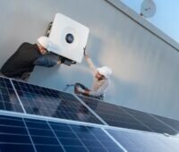 Im Bild zwei Männer, die einen Sunny Tripower X 60 Photovoltaik-Wechselrichter von SMA an eine Außenwand schrauben.