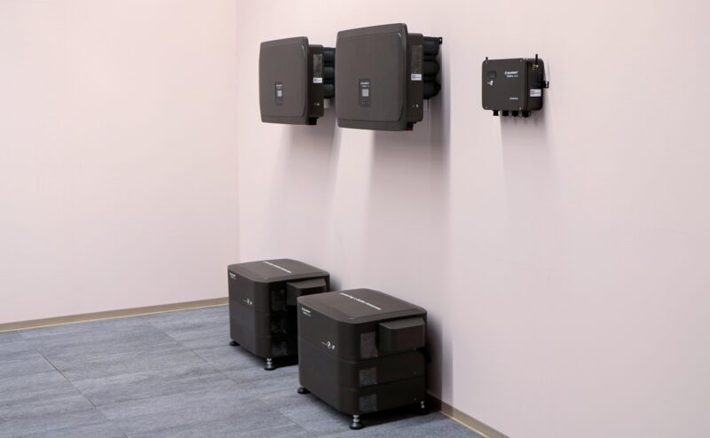 Schwarze Geräte an rosa Wand: Die Clusterbox von Solarwatt kann mehrere Batteriespeicher zu einem Gesamtsystem kombinieren.