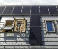 Zwei Menschen schauen aus Dachfenster zwischen Photovoltaikmodulen, Energy Sharing ist eine Alternative zur Einspeisevergütung von Solarstrom.