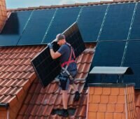 Ein Installateur auf dem Dach trägt ein Photovoltaik-Modul, ergonomische Solarmodule erleichtern das Handling.