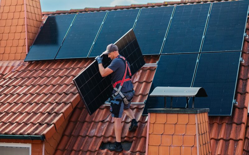 Ein Installateur auf dem Dach trägt ein Photovoltaik-Modul, ergonomische Solarmodule erleichtern das Handling.