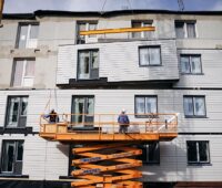 Ein Kran hebt Bauelemente an die Fassade, serielle Sanierung mit vorgefertigten Holzständerelementen.