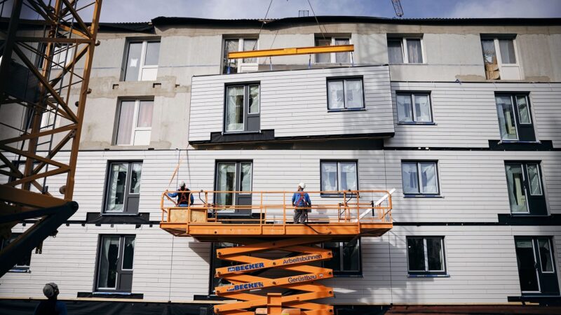 Ein Kran hebt Bauelemente an die Fassade, serielle Sanierung mit vorgefertigten Holzständerelementen.