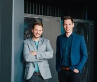 Laurenz Sutterlüty und David Riedl vor einem Enercube, einer Wärmepumpen-Heizzentrale für die Außenaufstellung.