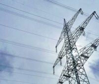 Der Blick durch einen Strommast in den Himmel, Forschende aus Jülich haben das Rätsel um die 60-Sekunden-Schwankung in Stromnetzen gelöst.