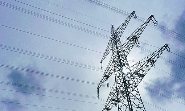 Der Blick durch einen Strommast in den Himmel, Forschende aus Jülich haben das Rätsel um die 60-Sekunden-Schwankung in Stromnetzen gelöst.