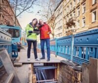 Zwei Menschen schauen in den Graben einer Wärmenetzbaustelle, Großwärmepumpen sollen in Wärmenetzen in Baden-Württemberg laut Netzwerk Großwärmepumpen vermehrt zum Einsatz kommen.