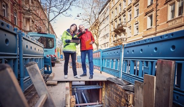 Zwei Menschen schauen in den Graben einer Wärmenetzbaustelle, Großwärmepumpen sollen in Wärmenetzen in Baden-Württemberg laut Netzwerk Großwärmepumpen vermehrt zum Einsatz kommen.