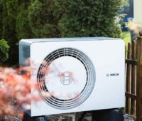 Eine Bosch-Wärmepumpe zwischen Blumen, intelligente Thermostate ermöglichen eine smarte Heizungssteuerung, die Photovoltaik-Anlage, Batteriespeicher und Wärmepumpe vernetzt.