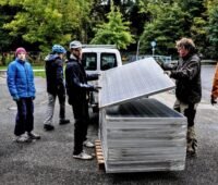 Ein Stapel gebauchte Solarmodule und Menschen, die diese für Balkonkraftwerke umrüsten.
