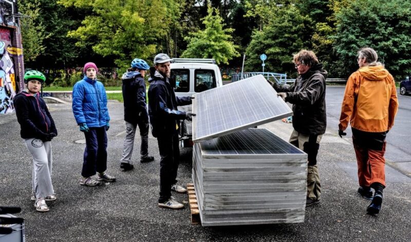 Ein Stapel gebauchte Solarmodule und Menschen, die diese für Balkonkraftwerke umrüsten.