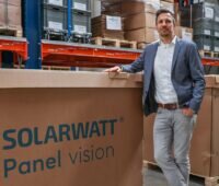 Im Bild Solarwatt-Produkt-Manager Gregor Kuschmann, der neben einem Karton mit der Aufschrift Panel Vision steht, das Unternehmen bietet leistungsstärkere TOPCon-Solarmodule an.