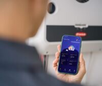 Eine Hand mit Handy, Spotmyenergy bindet Fronius-Wechselrichter in sein Heim-Energiemanagementsystem (HEMS) ein.