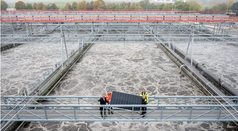 Offizielle zeigen ein Solarmodul auf einem Steg über dem Klärbecken, Stuttgarts größte Photovoltaik-Anlage entsteht als Faltdach über dem Hauptklärwerk.