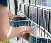Zwei Personen fädeln die flexiblen Solarmodule Vertical+ von Sunbooster in einem Doppelstabmattenzaum ein und bauen so eine Zaumsolaranlage.
