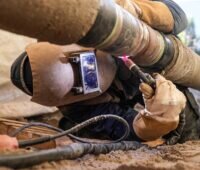 Ein Mann schweißt eine Stahlleitung, Stadtwerke Stuttgart bauen Wasserstoff-Pipeline für Green Hydrogen Hub.