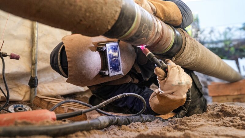 Ein Mann schweißt eine Stahlleitung, Stadtwerke Stuttgart bauen Wasserstoff-Pipeline für Green Hydrogen Hub.