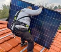 Ein Installateur auf dem Dach mit Solarmodul in den Händen trägt das Bionicback Exoskelett, das für Rückenentlastung bei der Photovoltaik-Montage sorgen soll.