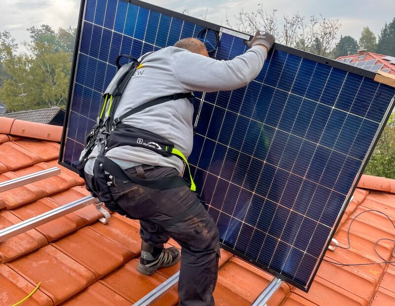 Ein Installateur auf dem Dach mit Solarmodul in den Händen trägt das Bionicback Exoskelett, das für Rückenentlastung bei der Photovoltaik-Montage sorgen soll.