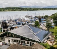 Der Hafenwirt mit BIPV-Solardach, im Hintergrund Segelyachten auf dem Chiemsee.