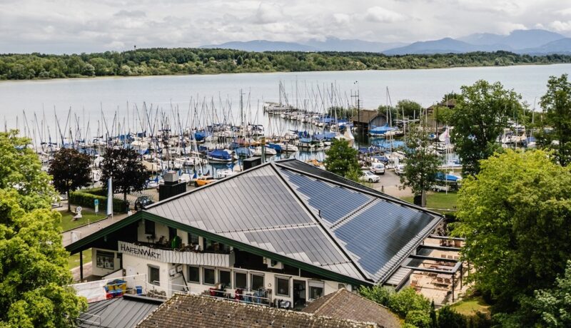 Der Hafenwirt mit BIPV-Solardach, im Hintergrund Segelyachten auf dem Chiemsee.