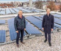 Zwei Männer lachend auf einem Flachdach mit Solaranlagen.