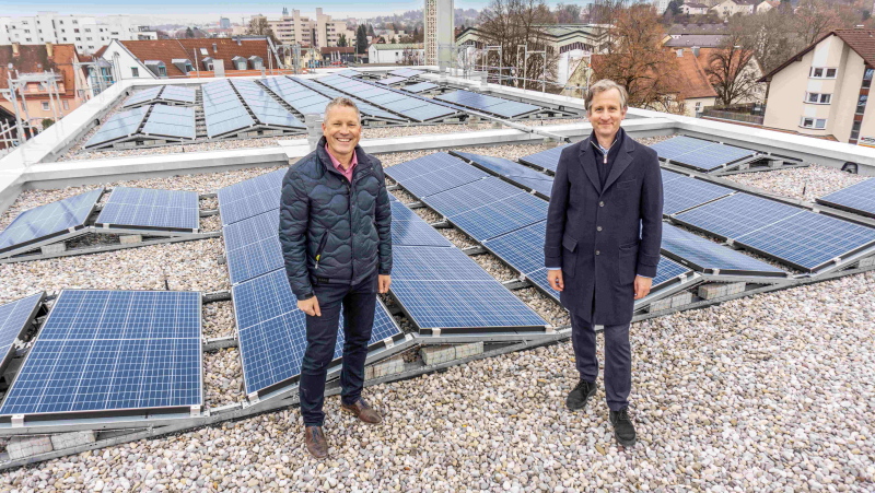 Zwei Männer lachend auf einem Flachdach mit Solaranlagen.