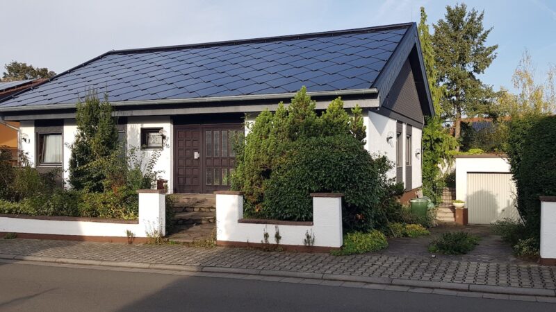 Einfamilienhaus von Martin Stoltenberg mit dunkelblauem, vollständig mit SunStyle-Solarziegeln gedecktem Satteldach, von der Straßenseite aufgneommen.