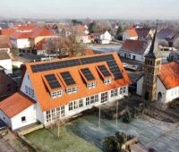 Luftbild einer Schule mit PV-Dach in einem Städtchen mit alter Kirche.