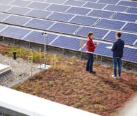 Eine PV-Dachanlage auf einem Flachdach, davor zwei Personen im Gespräch.