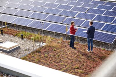 Eine PV-Dachanlage auf einem Flachdach, davor zwei Personen im Gespräch.