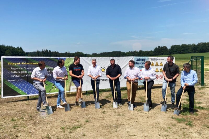 Spatenstich von 9 Personen auf Ackewrfläche vor Transparenten bei sonnigem Wetter.