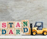 Spielzeug-Gabelstapler transportiert Würfel mit Schriftzug "Standard"-Symbol für einheitliche Wertschöpfungskette in der PV