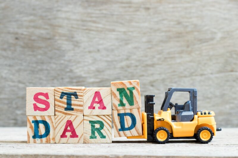 Spielzeug-Gabelstapler transportiert Würfel mit Schriftzug "Standard"-Symbol für einheitliche Wertschöpfungskette in der PV