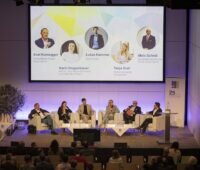 Podiumsdiskussion auf Pv-Konferenz in Österreich: 6 Menschen auf breiten Sesseln, Projektion mit Namen und Parteien