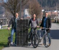 Drei Personen mit Fahrrädern auf einem Radweg mit einem großen Solarmodul