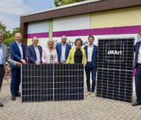 Gruppe von Menschen mit PV-Modulen vor Gebäude - Einweihung der ersten Photovoltaik-Anlage der Solaroffensive in Mannheim.
