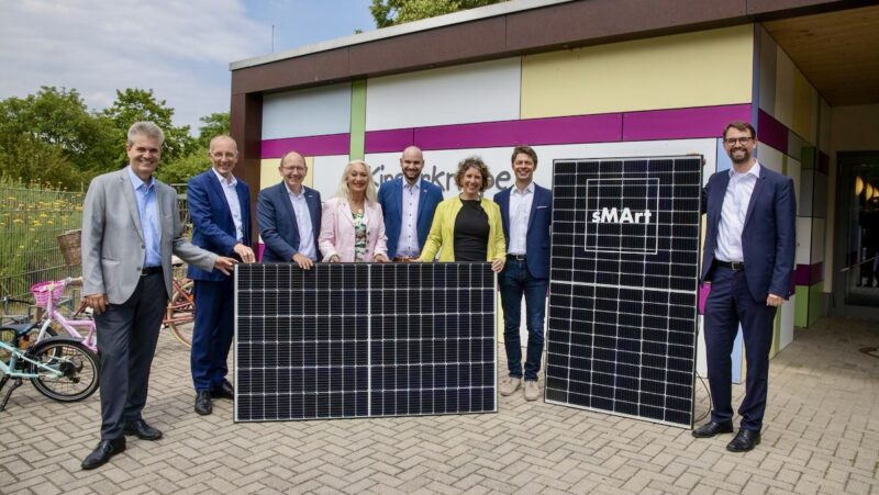 Gruppe von Menschen mit PV-Modulen vor Gebäude - Einweihung der ersten Photovoltaik-Anlage der Solaroffensive in Mannheim.