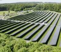 Luftaufnahme einer PV-Freiflächenanlage am Rande einer Autobahn und umschlossen von Bäumen.