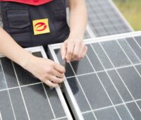 Zwei weibliche Hände mit Scharubenzieher über Solarmodulen.