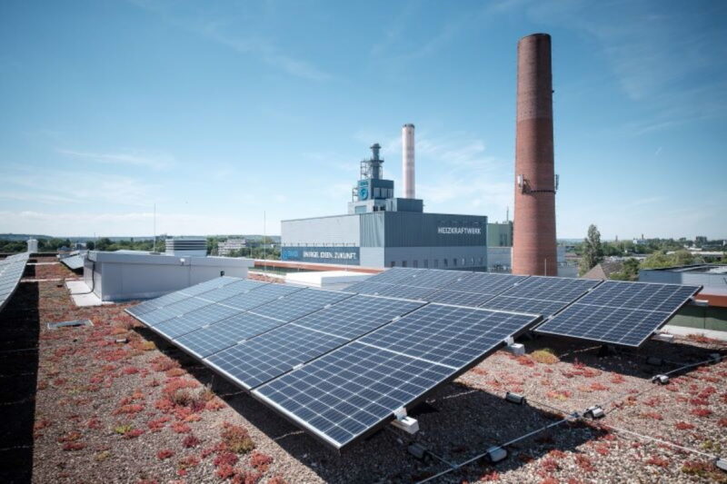 PV-Anlagen auf Flachdach vor Industrieschornsteinen.