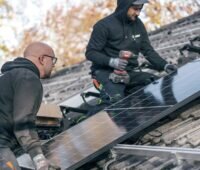 Im Bild zwei Handwerker auf dem Dach mit Solarmodul bei einer Installation vom Solar-Online-Anbieter Zolar.