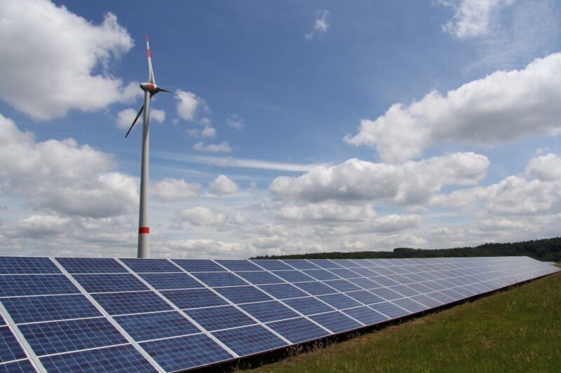 Eine PV-Freiflächen- und eine Windenergieanlage vor blauem wolkenreichen Himmel.