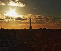 Paris mit Eifelturm vor teif stehender Sonne hinter Wolken