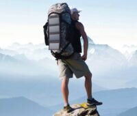 Im Bild ein Mann auf einer Bergspitze, der ein faltbares Photovoltaik-Panel auf dem Rucksack befestigt hat. Foto: Pearl GmbH