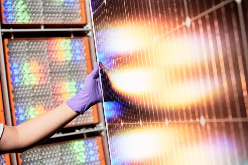 ein Ausschnitt aus Solarmodul, das von einer Hand gehalten wird und zwei Lichtflecken zeigt - das Perowskit-Tandem-Modul