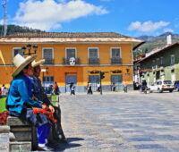Auf dem von den Spaniern einst gebauten Hauptplatz der peruanischen stadt Cajamarca sitzt ein indigenes Paar in traditioneller Ttacht. Im Hintergrund die Anden.